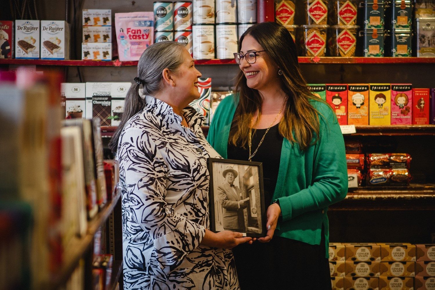 Two generations of the Hartley's family inside the Kingston shop, holding a framed photograph of an earlier keeper of the store